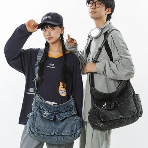 May include: Two people wearing denim messenger bags. One bag is light blue with the letter "B" on the front pocket, and the other is black with the letter "A". Both bags have multiple pockets and adjustable straps.