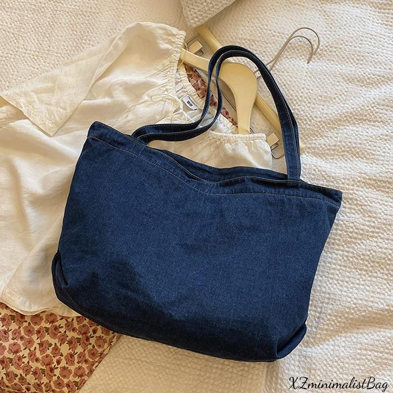 May include: A dark blue denim tote bag with two handles. The bag is rectangular with a slightly curved top edge. The text "XZminimalistBag" is visible in the bottom right corner. The bag is sitting on a white surface.