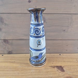 Può includere: Un portacandele cilindrico in ceramica con un design dipinto a mano nei toni mano nei toni mano nei toni del blu e del marrone. La superficie presenta fasce orizzontali sovrapposte decorate con spirali blu, un motivo a farfalla e un uccellino blu su un ramo.