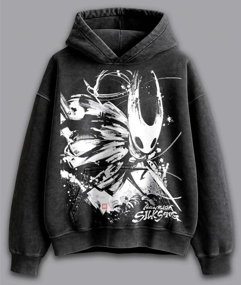 May include: Black hooded sweatshirt with a white and black graphic of a Hollow Knight character. The design includes the text "Hollow Knight Silksong". The sweatshirt has a kangaroo pocket and a drawstring hood.