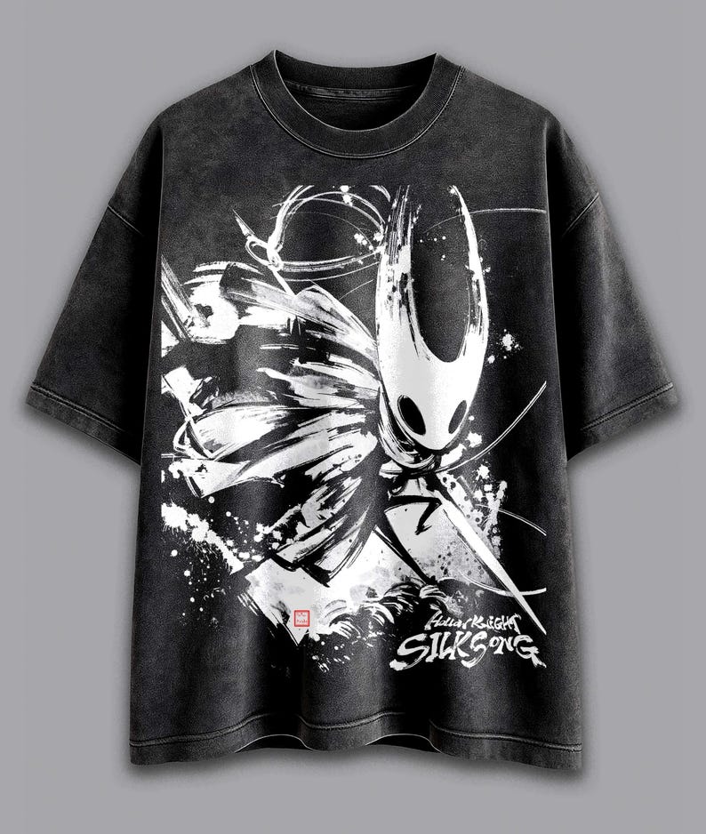 May include: Dark grey t-shirt with a white and black graphic of a character from the video game Hollow Knight. The graphic includes the text "Hollow Knight SILKSONG". The shirt has a vintage, washed appearance.