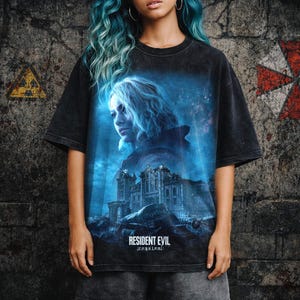 Könnte beinhalten: Schwarzes T-Shirt mit einem blau-weißen Resident Evil: Requiem-Motiv. Das Design zeigt ein Frauenporträt und ein gotisches Gebäude. Das T-Shirt hat einen Used-Look und der Text "RESIDENT EVIL requiem" ist unten aufgedruckt.