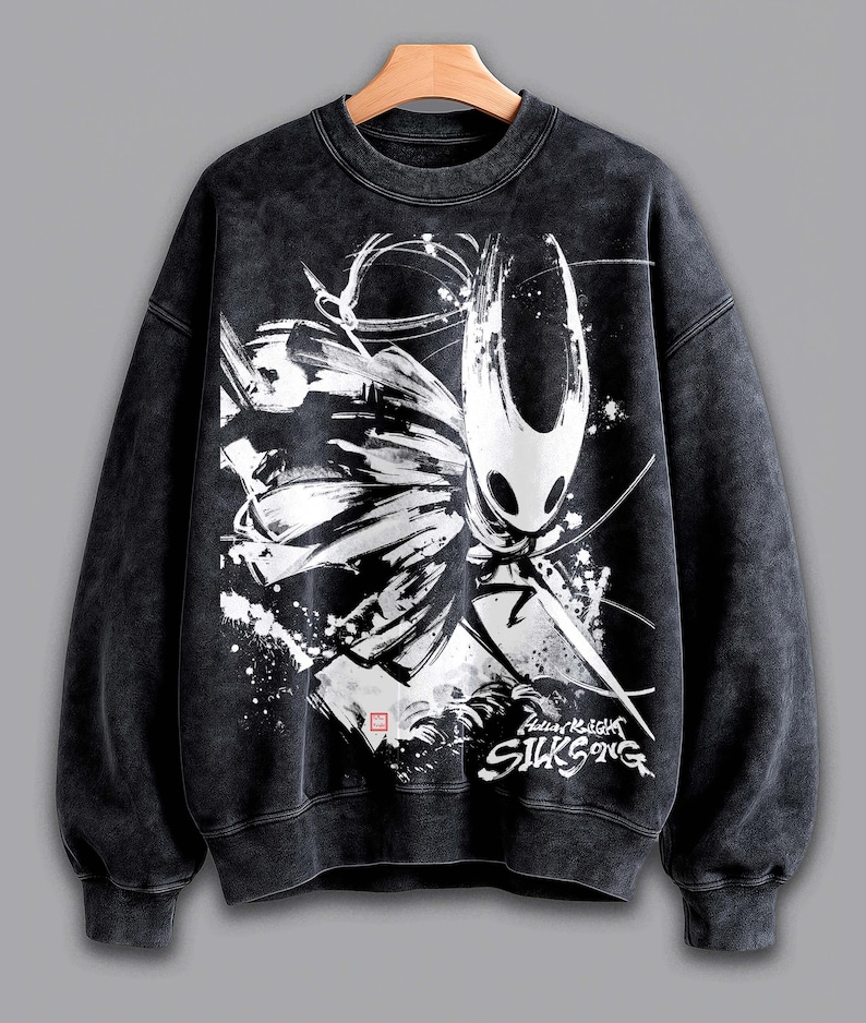 May include: Black sweatshirt with a white and black graphic of a character from the video game Hollow Knight. The graphic includes the text "Hollow Knight Silksong". The sweatshirt has a crew neck and long sleeves.