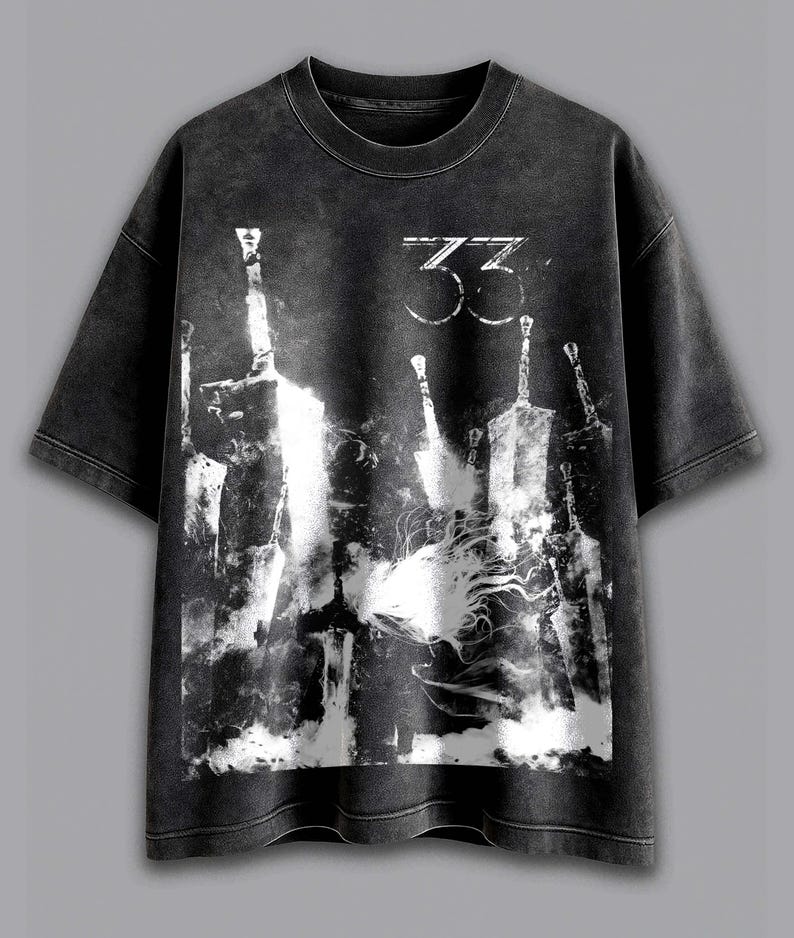 以下が含まれることがあります： 色あせたグラフィックプリントのダークグレーTシャツ。デザインは、様式化された剣と数字の「33」を白で表現しています。Tシャツはクルーネックと半袖です。
