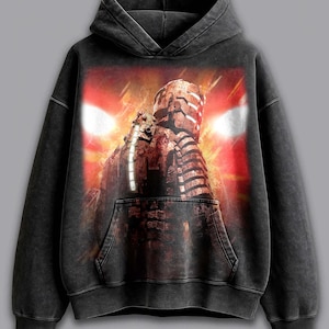 May include: Black hoodie featuring a graphic of a character with a helmet and glowing red lights. The design is set against a red and orange background. The hoodie has a kangaroo pocket and a drawstring hood.