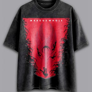 May include: Dark gray t-shirt with a red graphic. The graphic features the text "MAKE US WHOLE" at the top, with a central design of figures and lines. The shirt has a vintage, washed appearance.