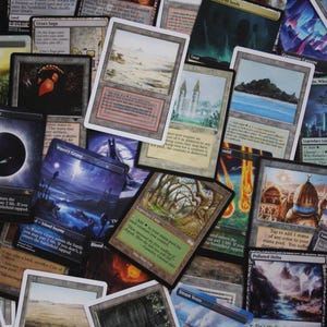 May include: A selection of Magic: The Gathering trading cards, showcasing diverse artwork and card designs. The cards feature a variety of colours, including blues, greens, and browns, with fantasy landscapes and abstract designs. The cards are arranged in a scattered, overlapping pattern.