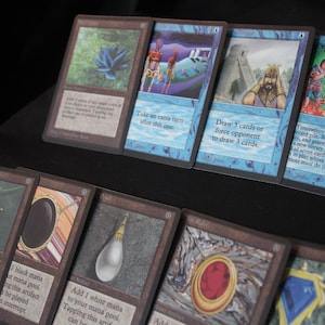 May include: A selection of Magic: The Gathering cards. The cards display illustrations and text, including a blue lotus, figures, and text such as "Draw 3 cards or force opponent to draw 3 cards."