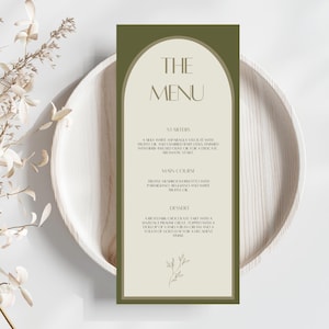 May include: An olive green menu card with the words "THE MENU" in a stylish font. The menu lists starters, main course, and dessert options. The menu is on a wooden plate. The menu card has a cream-colored arch shape.