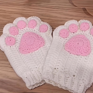 May include: A pair of white crochet gloves shaped like cat paws, with pink paw pads. The gloves are made of a soft, textured yarn and are designed to cover the hand and wrist.