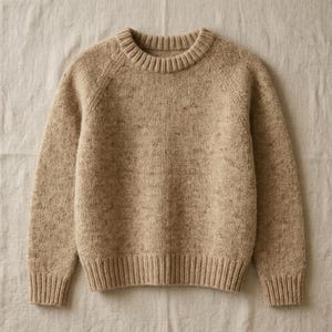 May include: A tan-colored sweater with a crew neck and ribbed cuffs and hem. The knitwear has a speckled texture, and the raglan sleeves are visible. The sweater is made of a soft, warm material, perfect for cooler weather.