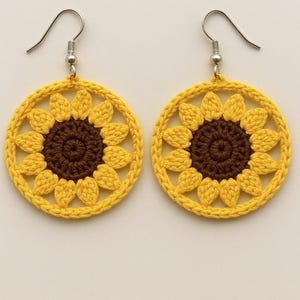 Puede incluir: Un par de pendientes de ganchillo hechos a mano con un diseño de girasol. Los pendientes presentan un anillo exterior amarillo con pétalos amarillos que rodean un centro marrón. Los pendientes cuelgan de alambres plateados.