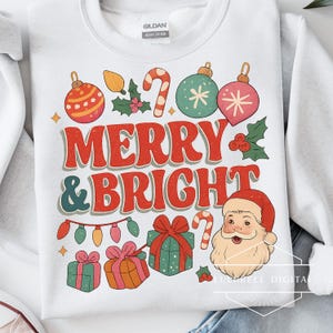 May include: White sweatshirt with a retro Christmas design. The design includes the words "MERRY & BRIGHT" in red, along with illustrations of ornaments, Santa Claus, gifts, and candy canes. The sweatshirt is made of heavy cotton.