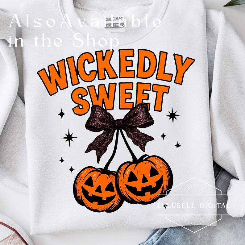 May include: White sweatshirt with the text "WICKEDLY SWEET" in orange, a dark purple bow, and two orange jack-o'-lanterns. The design includes black star accents, perfect for Halloween. Text at the top says "Also Available in the Shop".