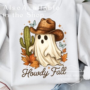 May include: White sweatshirt with a graphic of a ghost wearing a cowboy hat, a cactus, butterflies, and fall leaves. The text "Howdy Fall" is below the graphic. The words "Also Available in the Shop" are at the top.