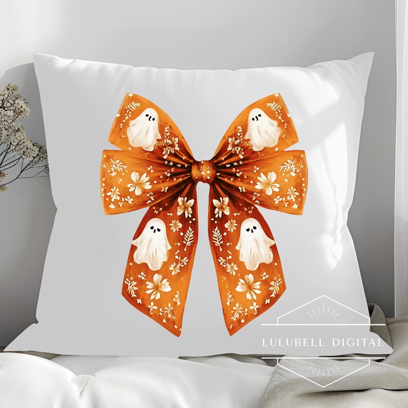 May include: White square pillow featuring a large orange bow design with white ghost illustrations and floral accents. The bow is centered on the pillow, creating a festive Halloween theme. The pillow is on a white surface.