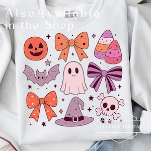 May include: White sweatshirt featuring a collection of Halloween-themed illustrations. The design includes a jack-o'-lantern, bows, a bat, a ghost, candy corn, a witch's hat, a skull, and stars. The text "Also Available in the Shop" is visible.
