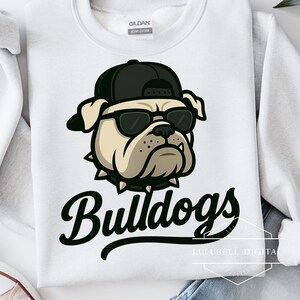 May include: White sweatshirt featuring a cartoon bulldog wearing a black cap and sunglasses. The bulldog has a spiked collar and the word "Bulldogs" in a stylized font below the graphic. The sweatshirt has a crew neck.
