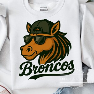 Puede incluir: Sudadera blanca con la imagen de una cabeza de caballo de dibujos animados con gafas de sol y una gorra de béisbol. La palabra "Broncos" está impresa en una fuente cursiva debajo del gráfico del caballo. La sudadera es de algodón grueso.