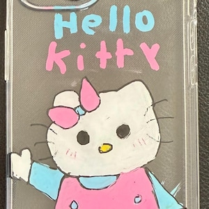 Puede incluir: Funda transparente para tel&eacute;fono con un dise&ntilde;o de Hello Kitty dibujado a mano. El dise&ntilde;o incluye un gato blanco con un lazo rosa, un vestido rosa y detalles azules. Las palabras "Hello Kitty" est&aacute;n escritas en azul y rosa.