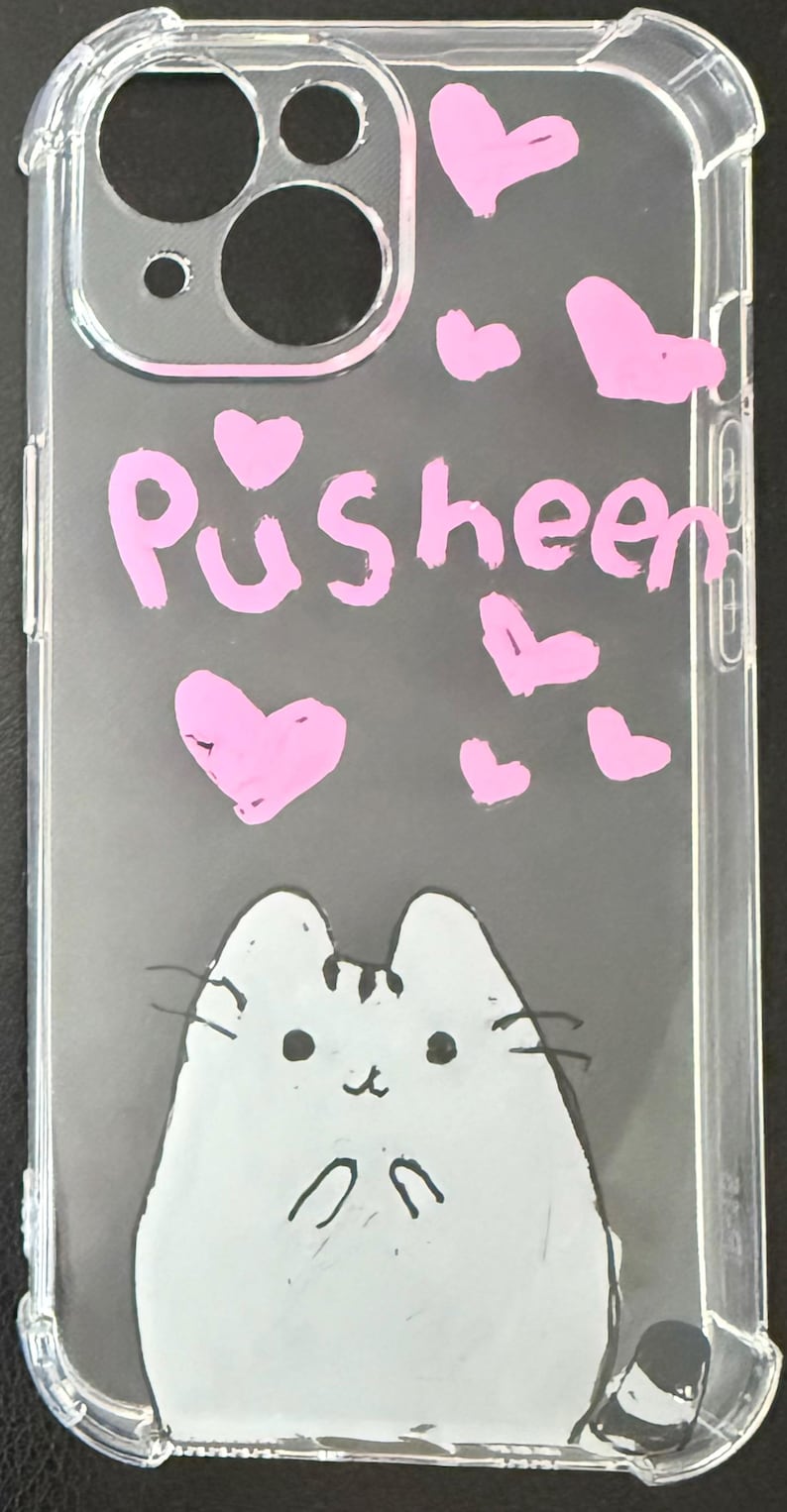 Puede incluir: Funda transparente para tel&eacute;fono con una ilustraci&oacute;n de gato de dibujos animados y la palabra "Pusheen" en rosa. Corazones rosas est&aacute;n dispersos por la funda. La funda tiene un parachoques protector en los bordes.