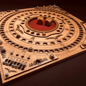 Può includere: Gioco da tavolo in legno con un design circolare, con motivi incisi, tra cui uccelli e frecce. Il tabellone ha più fori per sfere di metallo e due dadi. Il centro ha un inserto in feltro rosso. Il tabellone è in legno chiaro.