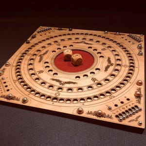 Könnte beinhalten: Ein Holzbrettspiel mit konzentrischen kreisförmigen Bahnen und geätzten Designs. Das Spiel verfügt über zwei Würfel und kleine Metallkugeln. Die Mitte des Bretts hat einen roten Filzeinsatz.