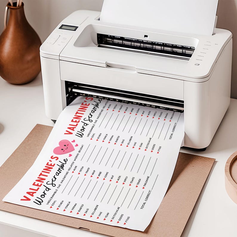 May include: A white printer printing a Valentine's Day word scramble game sheet. The sheet has the title "Valentine's Word Scramble" with a heart graphic. The game is designed to unscramble Valentine-related words. The printer is on a white surface.