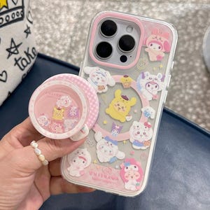 Puede incluir: Una funda transparente para teléfono con borde rosa y un pop socket a juego. La funda presenta pegatinas de personajes de dibujos animados. El pop socket tiene un patrón de cuadros rosa y blanco y contiene pequeñas figuras de personajes. El texto "OWOCASE" es visible.