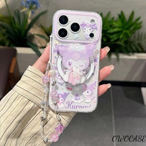 Puede incluir: Una funda transparente para teléfono con un diseño de dibujos animados morado y blanco con el personaje Kuromi. La funda tiene un soporte de anillo y una correa de muñeca con cuentas rosas y transparentes. La funda tiene el texto "Kuromi".