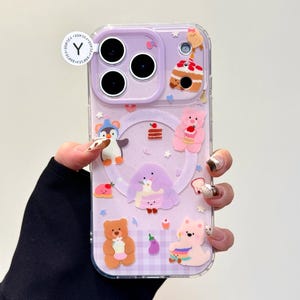 May include: A clear phone case with a purple backing featuring various cartoon characters and food items. The case has a penguin, bears, cake, and other cute designs. The case has a clear border and a small white sticker with a "Y" on it.