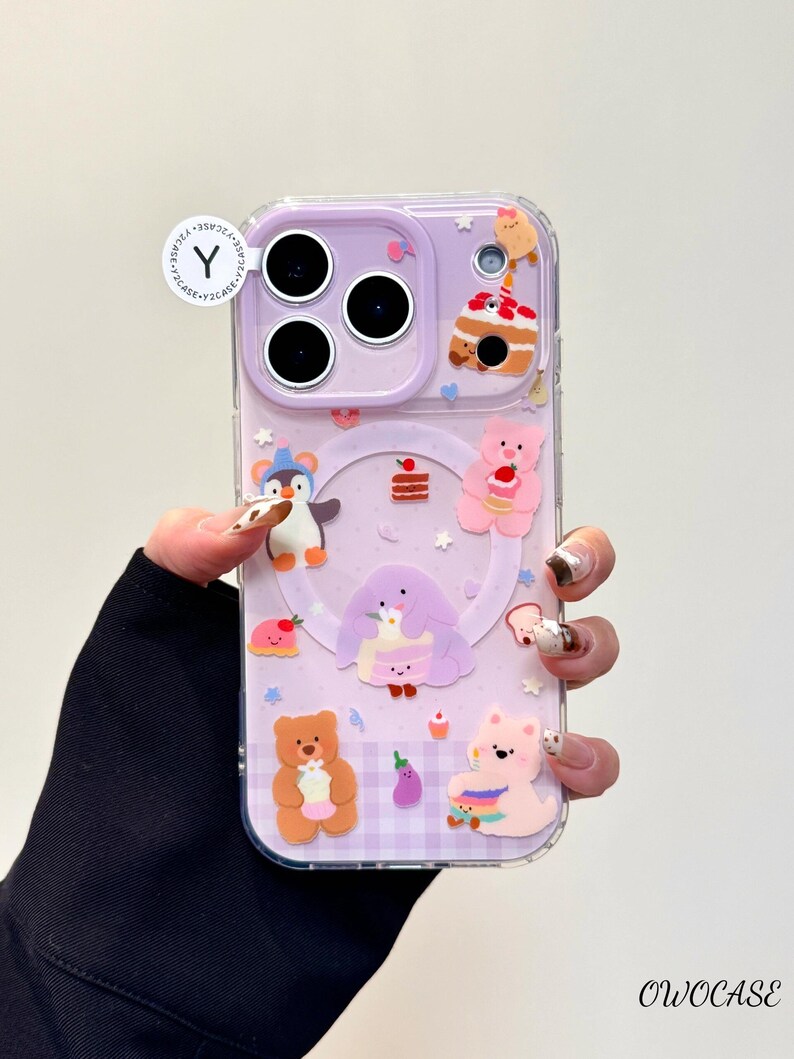 May include: A clear phone case with a purple backing featuring various cartoon characters and food items. The case has a penguin, bears, cake, and other cute designs. The case has a clear border and a small white sticker with a "Y" on it.
