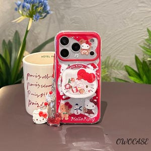 May include: Red and clear phone case featuring Hello Kitty characters. The case has a red border and a clear back with various Hello Kitty designs. A charm with a Hello Kitty head and a heart is attached. The text "Hello Kitty" is visible.