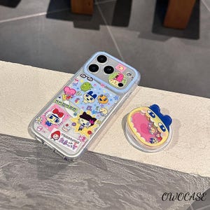 May include: A clear phone case with a light blue border and colorful cartoon character stickers. A matching phone grip is next to the phone case. The phone case and grip have a cute, playful design.