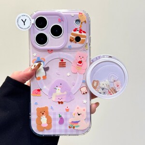 May include: A clear phone case with a purple backing featuring cartoon characters and food designs. The case has a clear, round, floating charm compartment. The case has the text "OWOCASE".