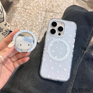 May include: A clear phone case with a star pattern and a matching pop socket featuring a Hello Kitty design. The pop socket has a blue gingham border. The phone case has a circular magnetic charging area.