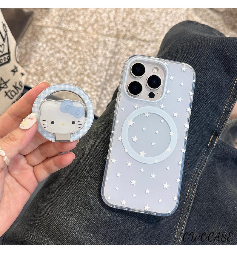 May include: A clear phone case with a star pattern and a matching pop socket featuring a Hello Kitty design. The pop socket has a blue gingham border. The phone case has a circular magnetic charging area.
