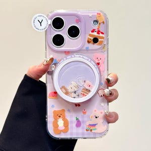 May include: A clear phone case with a purple background and a variety of cute, colorful bear and cake-themed decorations. The case has a pop-up grip with floating glitter and charms. The brand name "OWOCASE" is printed on the bottom right.