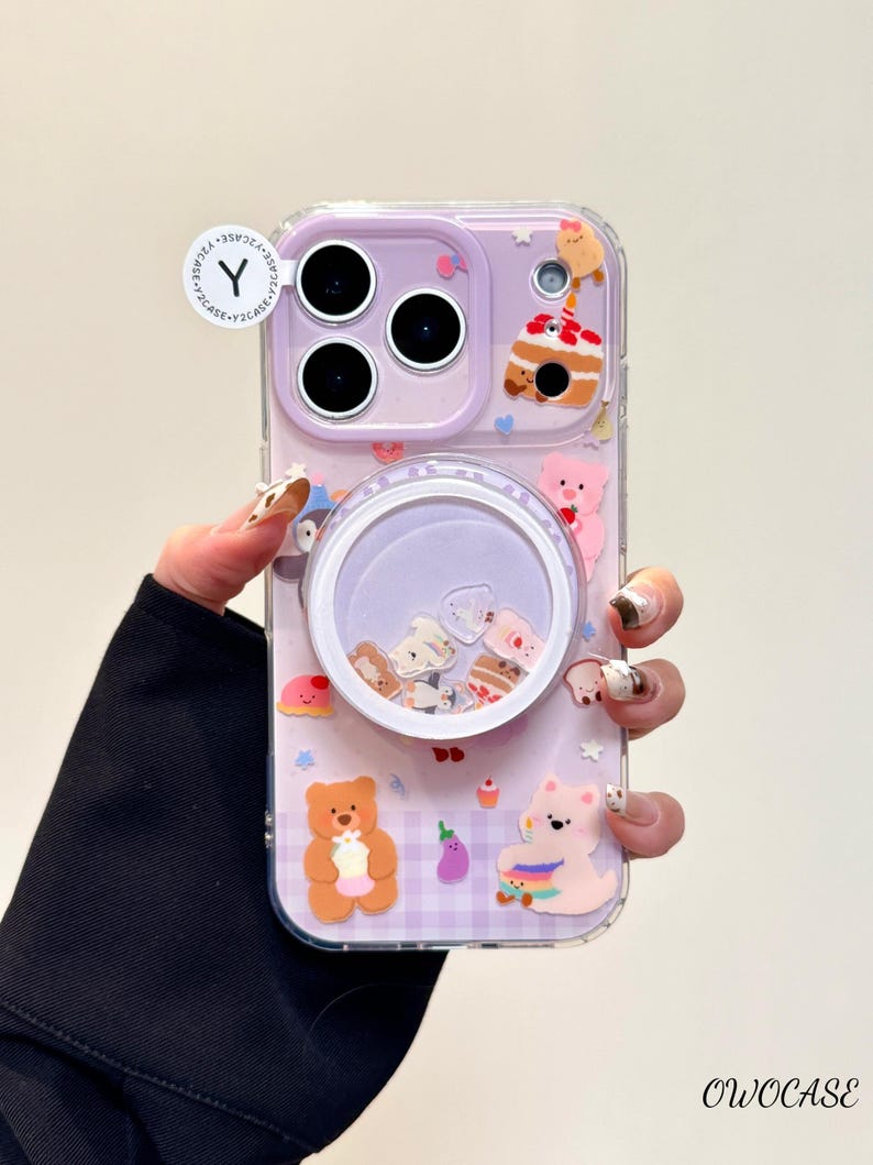 May include: A clear phone case with a purple background and a variety of cute, colorful bear and cake-themed decorations. The case has a pop-up grip with floating glitter and charms. The brand name "OWOCASE" is printed on the bottom right.
