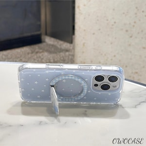 May include: A clear phone case with a light blue background and white star pattern. The case has a built-in ring holder with a gingham pattern and a kickstand. The phone case has the text "OWOCASE" at the bottom.