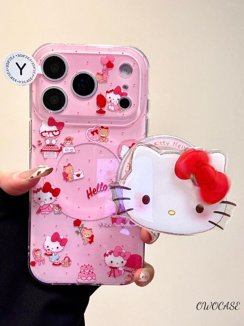 Pu&ograve; includere: Custodia per telefono rosa con sovrapposizione trasparente, con grafiche di Hello Kitty e orsetti. La custodia ha un design circolare trasparente con la scritta "Hello" in rosa. Un ciondolo separato di Hello Kitty &egrave; tenuto davanti.