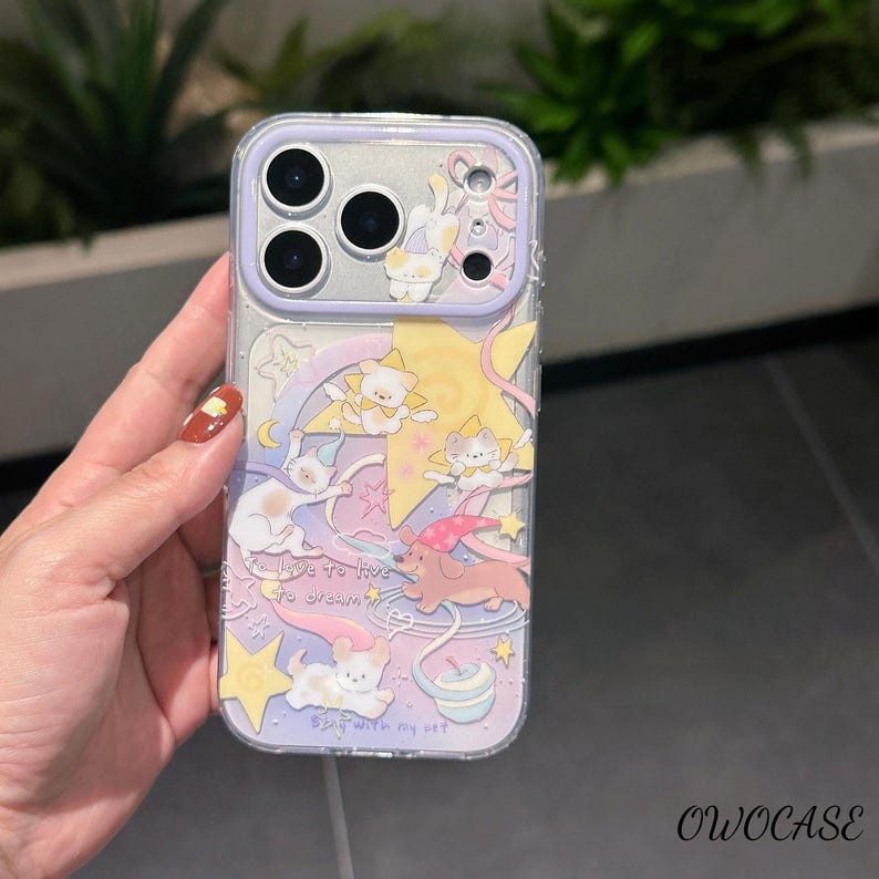 May include: Clear phone case with a whimsical design featuring cartoon cats, stars, and a pink and purple colour scheme. The case has a lavender border and the text "To live to dream, Stay with my cat."