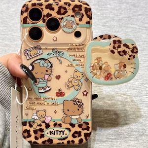 May include: A clear phone case with a leopard print design and Hello Kitty illustrations. The case features a detachable Hello Kitty head with floating glitter and small figures. Text includes "In winter, plush bears, sweet hot cocoa are needed" and "Kitty."