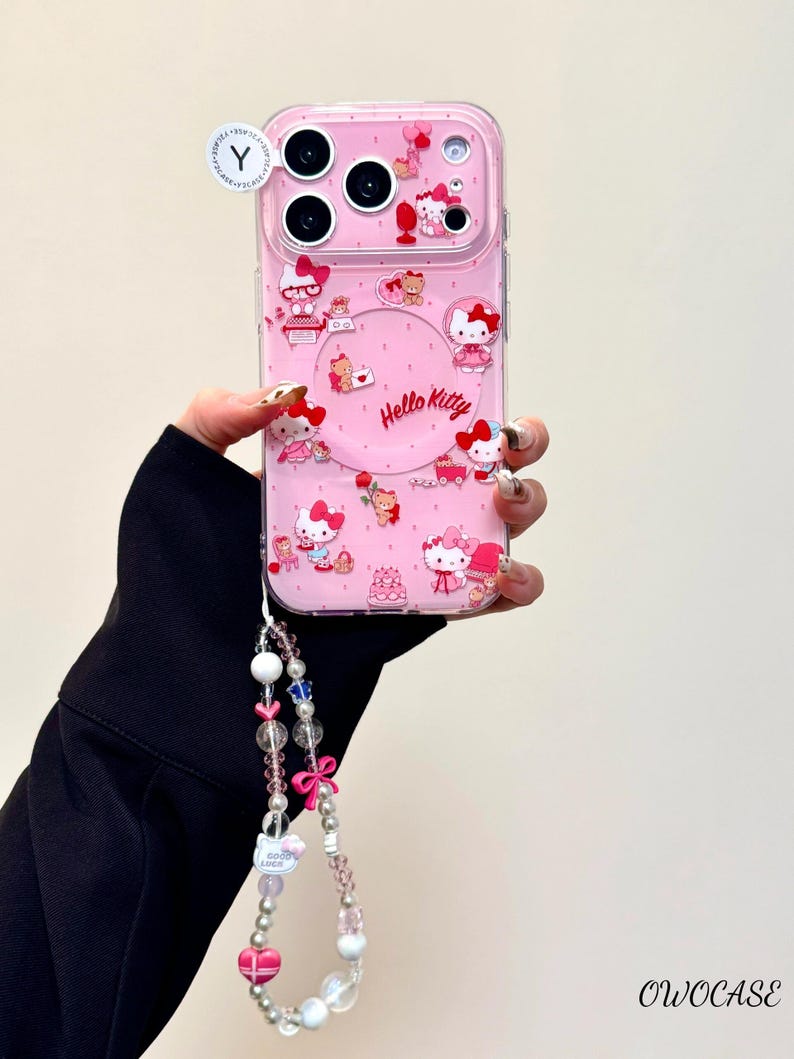 Pu&ograve; includere: Custodia per telefono rosa con disegni di Hello Kitty e cinturino da polso con perline. La custodia presenta diverse illustrazioni di Hello Kitty e le parole "Hello Kitty" in un design circolare. Il cinturino da polso include perline rosa, bianche e trasparenti e un fiocco rosa.