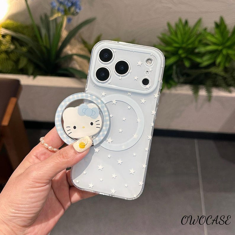 May include: A light blue phone case with a star pattern and a Hello Kitty ring holder. The case has a clear, protective design and features a magnetic ring for easy grip. The ring holder has a blue and white checkered pattern.