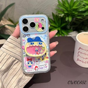 May include: Clear phone case with a blue border and colorful cartoon stickers. The stickers include a character with a blue hat and yellow mouth, a Hello Kitty sticker, and Japanese text. The case has a camera cutout and the text "OWOCASE".