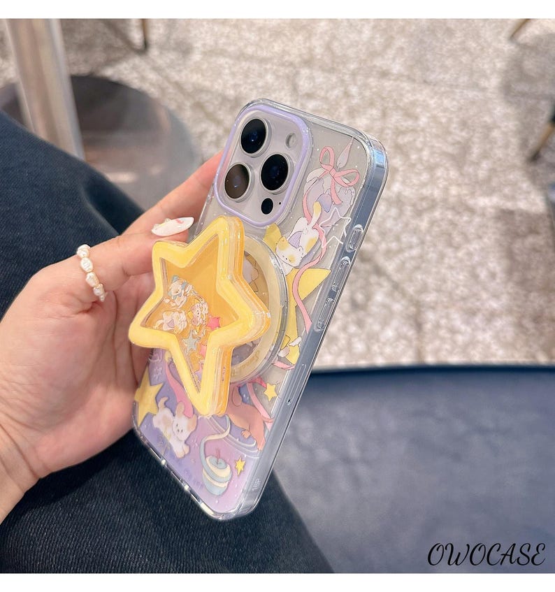 May include: Transparent phone case with a cartoon design and a yellow star-shaped phone grip. The case features a purple and yellow background with cartoon characters and the text "OWOCASE" at the bottom.