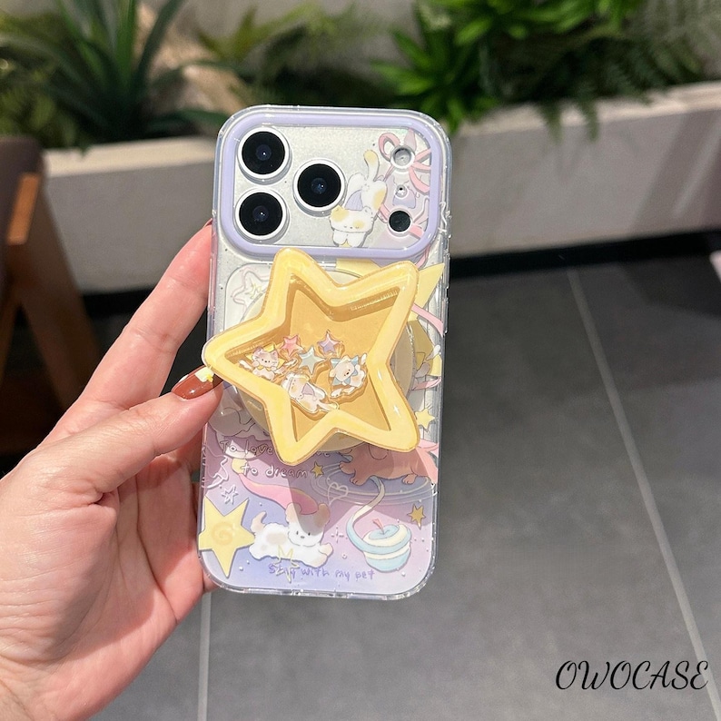 May include: Clear phone case with a whimsical design featuring a yellow star-shaped pop socket. The case has a lilac border and a pastel illustration of a cat, stars, and clouds. The text "Stay with my pet" is visible.