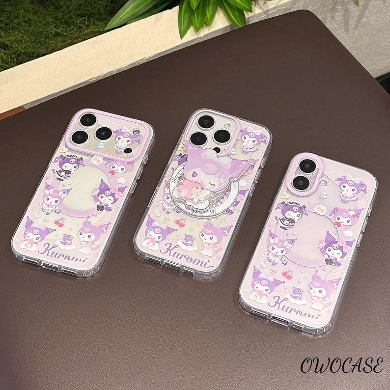 Puede incluir: Tres fundas transparentes para tel&eacute;fono con un dise&ntilde;o de Kuromi en morado y blanco. Cada funda presenta una disposici&oacute;n diferente de personajes de Kuromi, cerezas y la palabra "Kuromi". Las fundas tienen un borde transparente y est&aacute;n sobre una superficie marr&oacute;n.