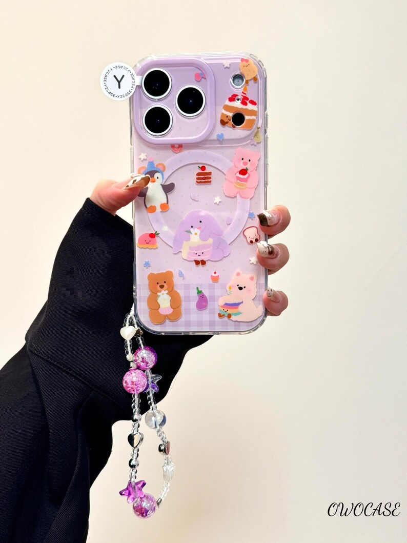 May include: A clear phone case with a lavender background and cartoon bear, penguin, and cake designs. The case has a decorative strap with pink and clear beads. The text "OWOCASE" is visible.